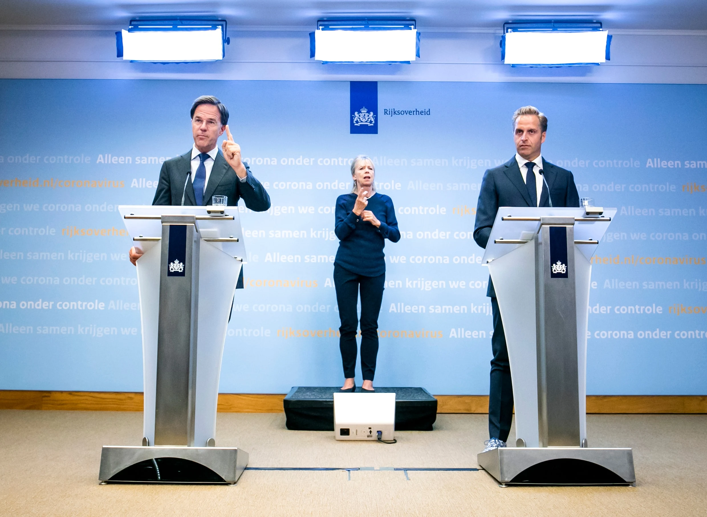 Toenmalig minister-president Mark Rutte en minister Hugo de Jonge tijdens een coronapersconferentie, met een gebarentolk tussen hen in.